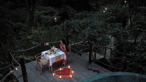 A wooden deck with a table set for two, surrounded by lush greenery and a heart-shaped flower arrangement. - Alamora Healing Escape (Sebatu)