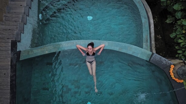 A person in a swimming pool with a curved edge and a stone border. - Alamora Healing Escape (Sebatu)