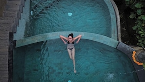 A person in a swimming pool with a curved edge and a stone border. - Alamora Healing Escape (Sebatu)