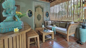 A wooden reception desk with a statue, a sofa, and a coffee table in a room with a tiled floor and a wooden ceiling. - Alamora Healing Escape (Sebatu)