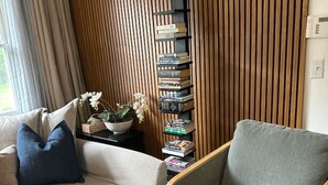 A living room with a sofa, armchair, and a tall bookshelf against a wooden wall. - Modern 1 bedroom apartment near Stony Brook university hospital walking distance (Stony Brook)