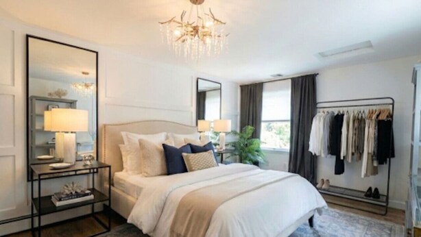 A bedroom with a bed, bedside tables, a mirror, a chandelier, a clothing rack, and a window with curtains. - Modern 1 bedroom apartment near Stony Brook university hospital walking distance (Stony Brook)