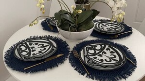 A round table with a white surface, surrounded by four blue placemats with black designs, a white bowl, and a potted plant with green leaves and white flowers. - Modern 1 bedroom apartment near Stony Brook university hospital walking distance (Stony Brook)