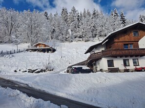A snow-covered landscape with two wooden cabins, one with a balcony and a car parked in front. - Pension Razil (Ladis)
