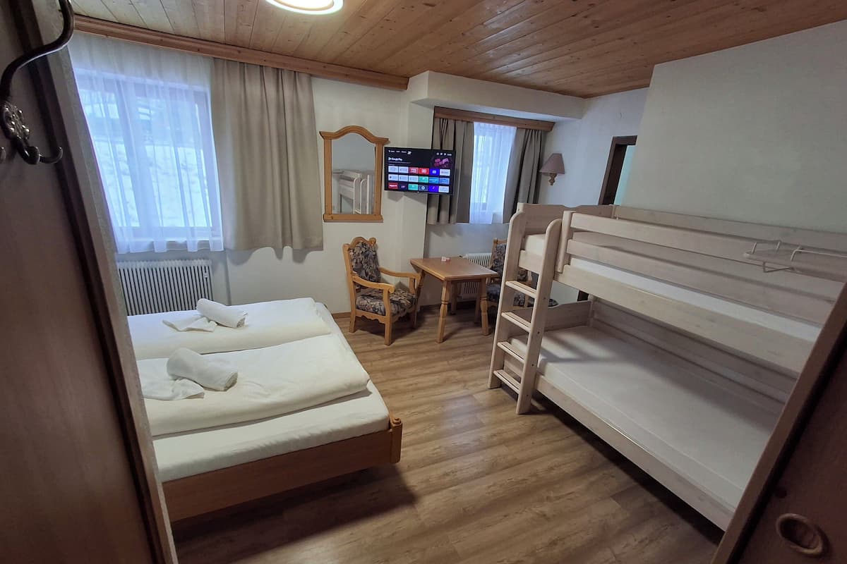 Ein Hotelzimmer mit einem Holzbett, einem Etagenbett aus Holz, einem Schreibtisch, einem Stuhl, einem Fernseher und einem Fenster mit Vorhängen.