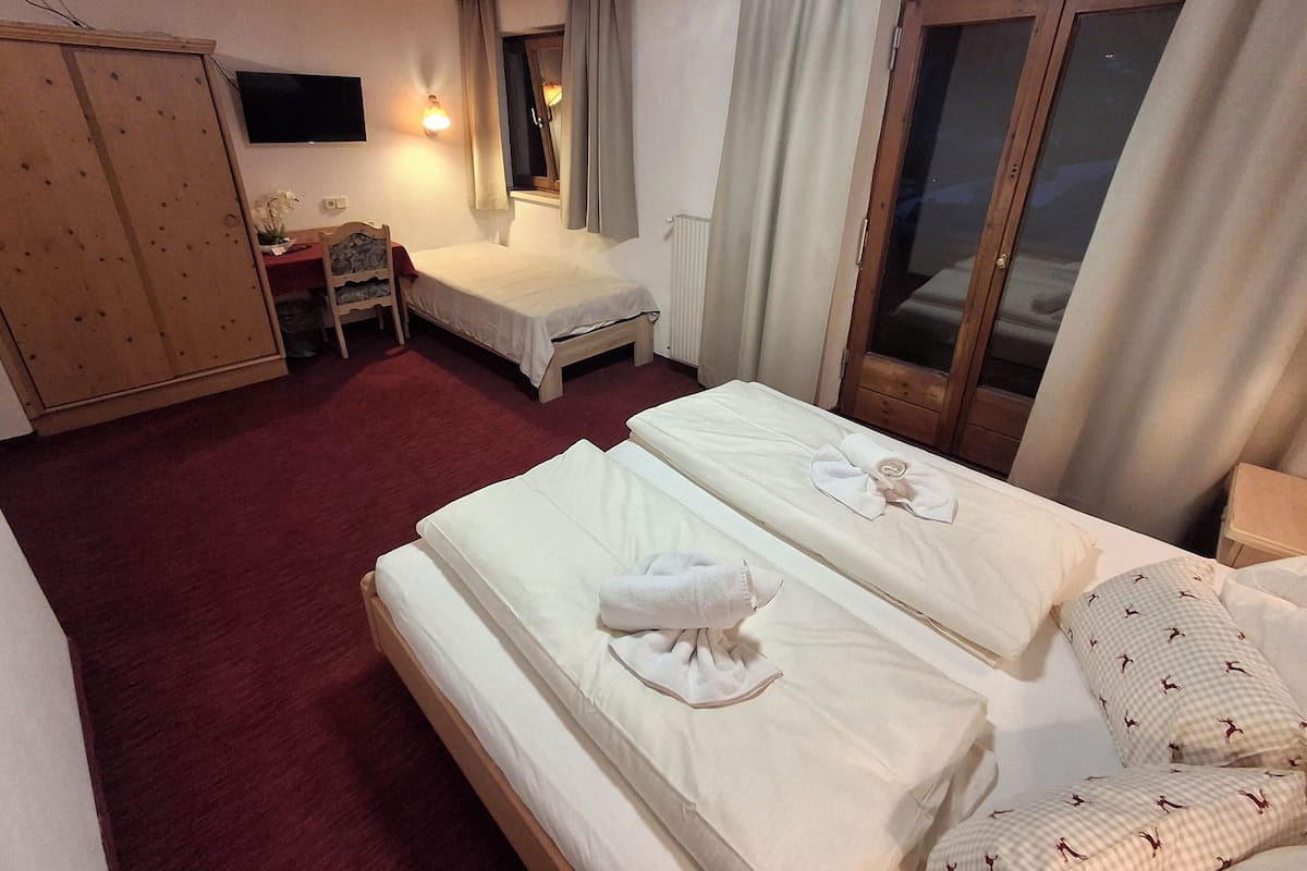 Ein Hotelzimmer mit zwei Betten, einem Holzschrank, einem Schreibtisch mit Stuhl, einem Fernseher und einem Fenster mit Vorhängen.