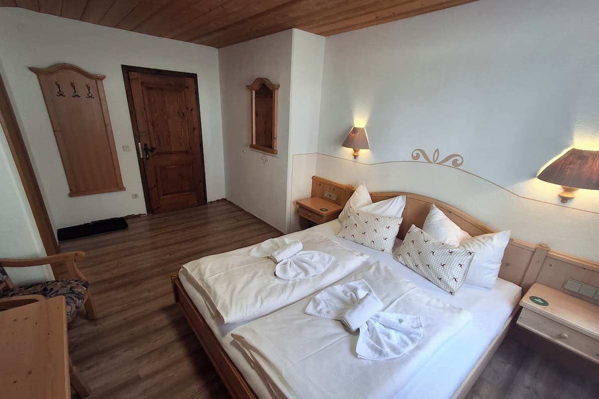 Ein ordentlich bezogenes Doppelbett mit weißen Leinen und dekorativen Kissen, ein hölzernes Kopfende, Nachttischlampen und ein Holzschrank.