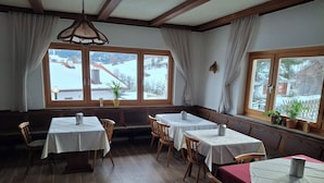 Un espace repas avec des tables et des chaises en bois, de grandes fenêtres avec des rideaux et une vue sur un paysage enneigé.