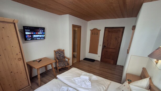 Une chambre d’hôtel avec un plafond en bois, un téléviseur fixé au mur, un bureau avec une chaise et un lit recouvert de draps blancs impeccablement tendus.