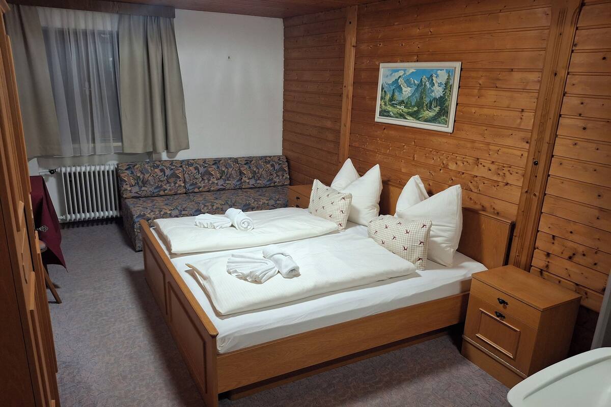 Ein Zimmer mit Holzwänden, einem Bett, einer Schlafcouch und einem kleinen Nachttisch.