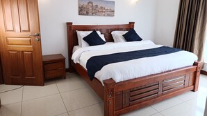 Une chambre à coucher avec un lit en bois, du linge de lit blanc, une table de chevet et un tableau accroché au mur.
