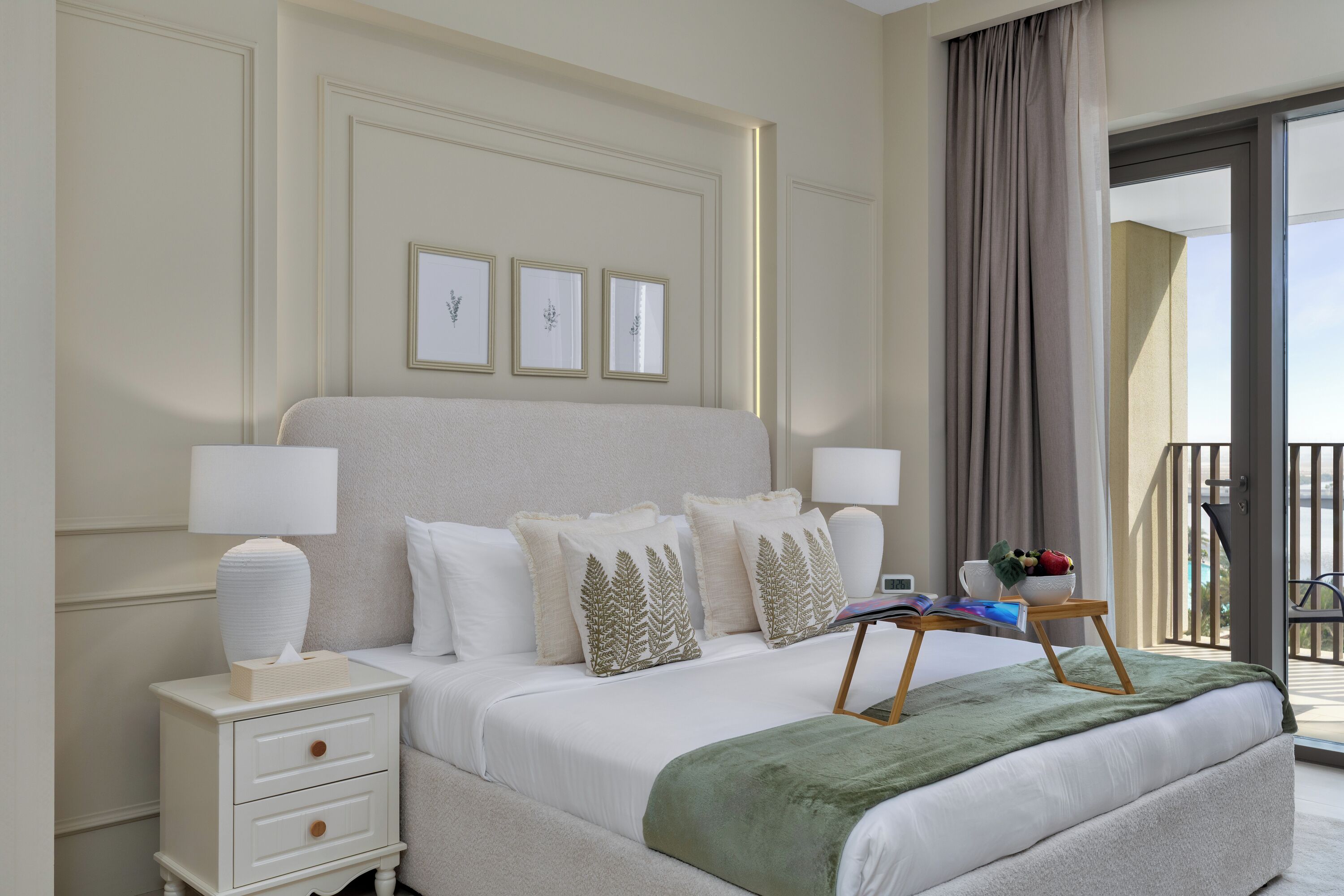 Ein ordentlich eingerichtetes Hotelzimmer mit einem großen Bett, Nachttischlampen, einem kleinen Tisch mit einem Buch und einer Obstschale sowie einem Balkon mit Blick.