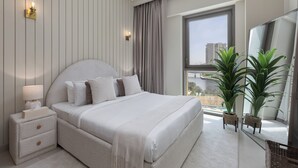 A modern bedroom with a large bed, bedside tables, a nightstand, a window with a view, and two potted plants. - Maison Privee - Creekside Elegance w/ Canal Vws at Creek Beach (Dubai)