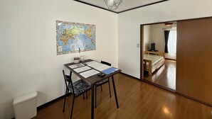 Ein Zimmer mit Holzboden, einem Esstisch mit Unterlagen, einem Stuhl, einer Karte an der Wand und einer Tür zu einem weiteren Raum.