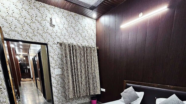 A modern bedroom with a large bed, dark wooden paneling, a mirror, and a patterned curtain. - Shree Kalyan Palace (Danta Ramgarh)