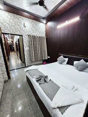 A modern bedroom with a large bed, dark wooden paneling, a mirror, and a patterned curtain. - Shree Kalyan Palace (Danta Ramgarh)