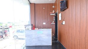 A reception desk with a marble top, wooden panel walls, a mounted TV, and a view of parked vehicles outside. - Shree Kalyan Palace (Danta Ramgarh)