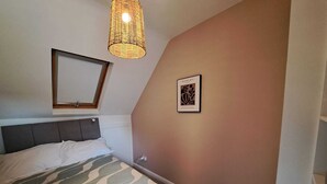 Un dormitorio con cama, lámpara colgante, una obra de arte enmarcada y ventana con marco de madera.