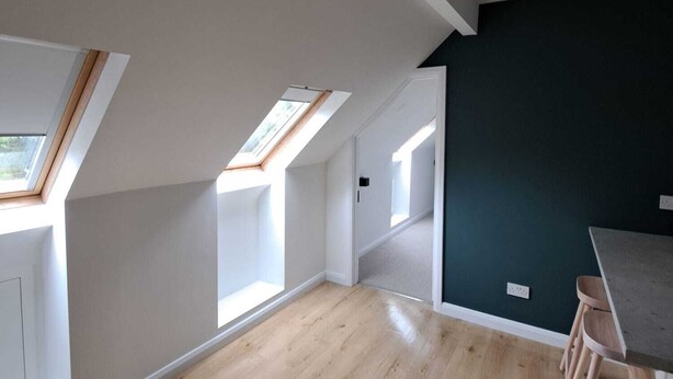 Una habitación amplia con suelo de madera, tragaluces y una pared de acento oscura.