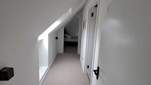 Un pasillo estrecho y bien iluminado con paredes blancas y piso alfombrado, que conduce a una habitación con literas.