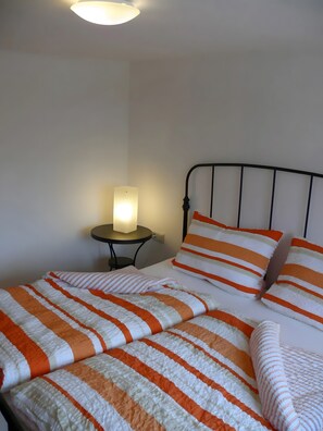 Un lit avec une literie à rayures, une table de chevet avec une lampe et un mur uni.