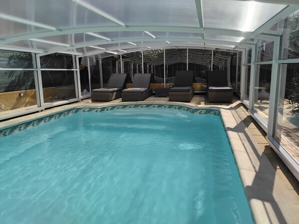 A covered swimming pool with lounge chairs and a glass enclosure.