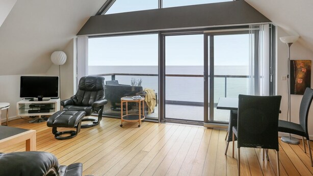 Un salón moderno con un gran ventanal que da a un balcón con vistas al mar.