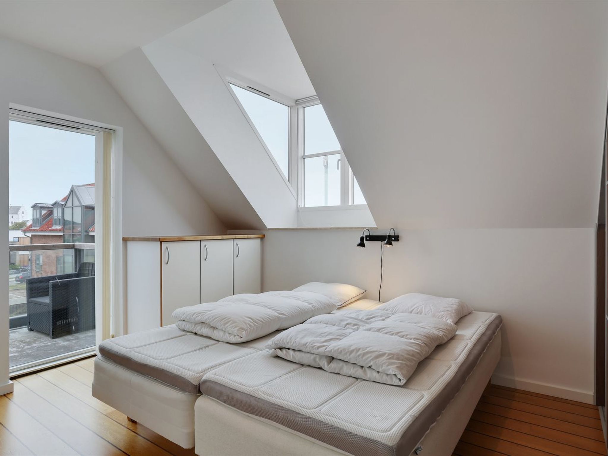 A bedroom with a sloped ceiling, a bed with white bedding, a small table, and a window.