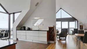Una cocina moderna con una isla grande, un comedor con una mesa alta y vistas a la ciudad a través de amplias ventanas.