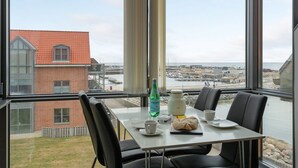 Comedor con una mesa preparada para dos, con vista a un puerto con barcos y edificios.