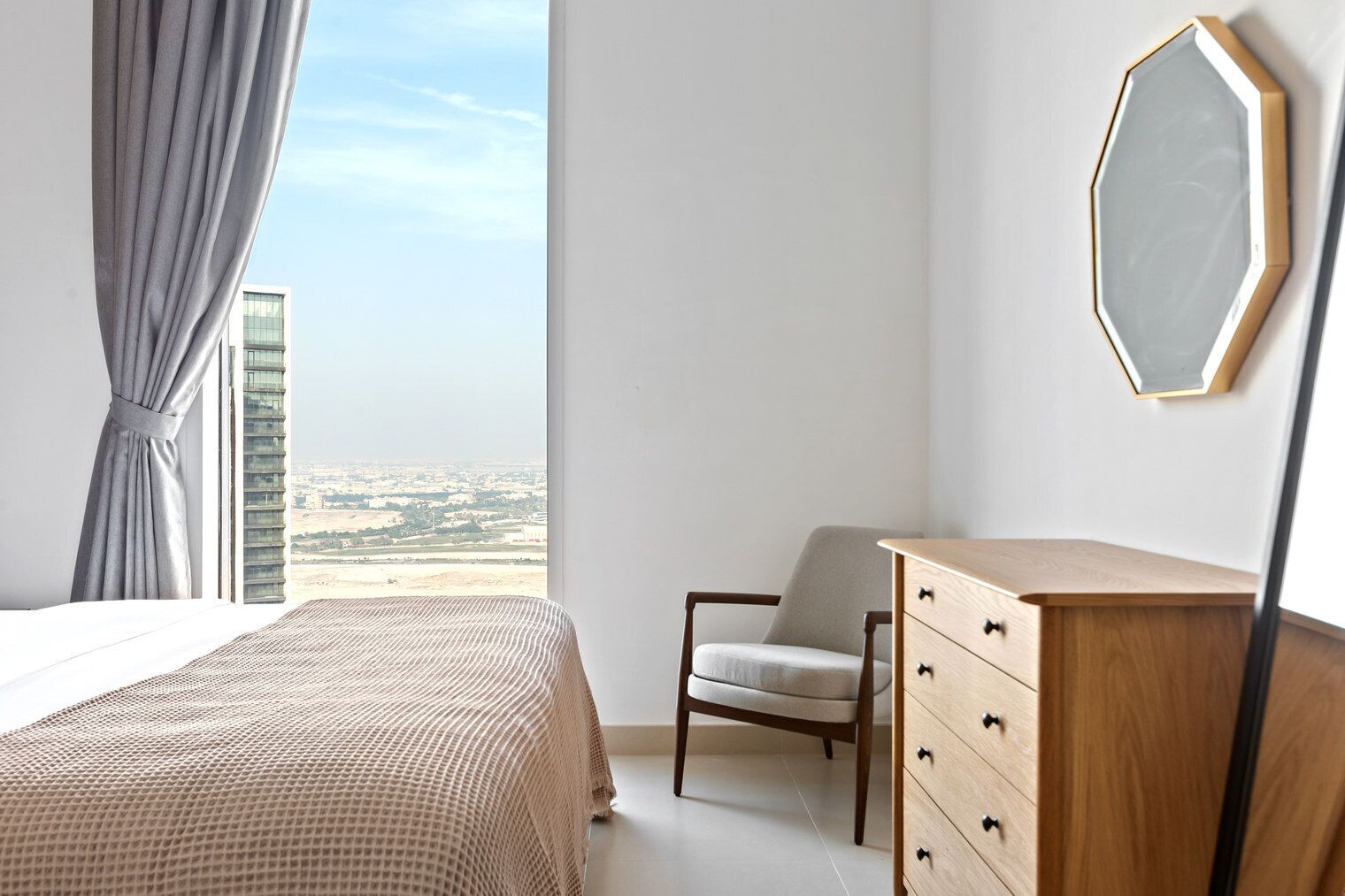 Ein Schlafzimmer mit Bett, Stuhl, Kommode und großem Fenster mit Blick auf die Stadt.