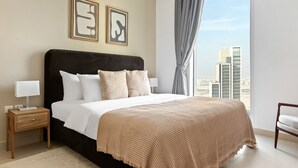 A modern hotel bedroom with a large bed, a nightstand, a chair, and a view of the cityscape.