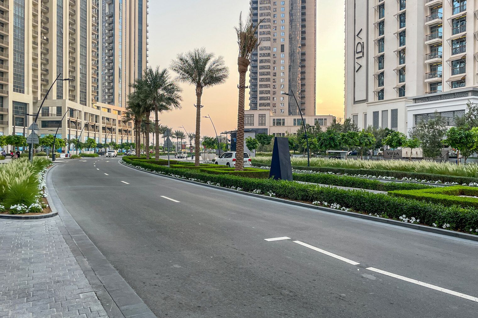 A wide, empty road flanked by high-rise buildings and palm trees, with a clear sky.