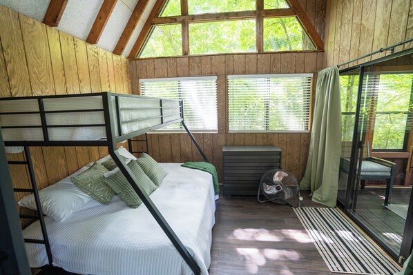 Habitación con literas, techo de madera, ventana con persianas, ventilador y puerta corredera de vidrio que da a un espacio exterior.