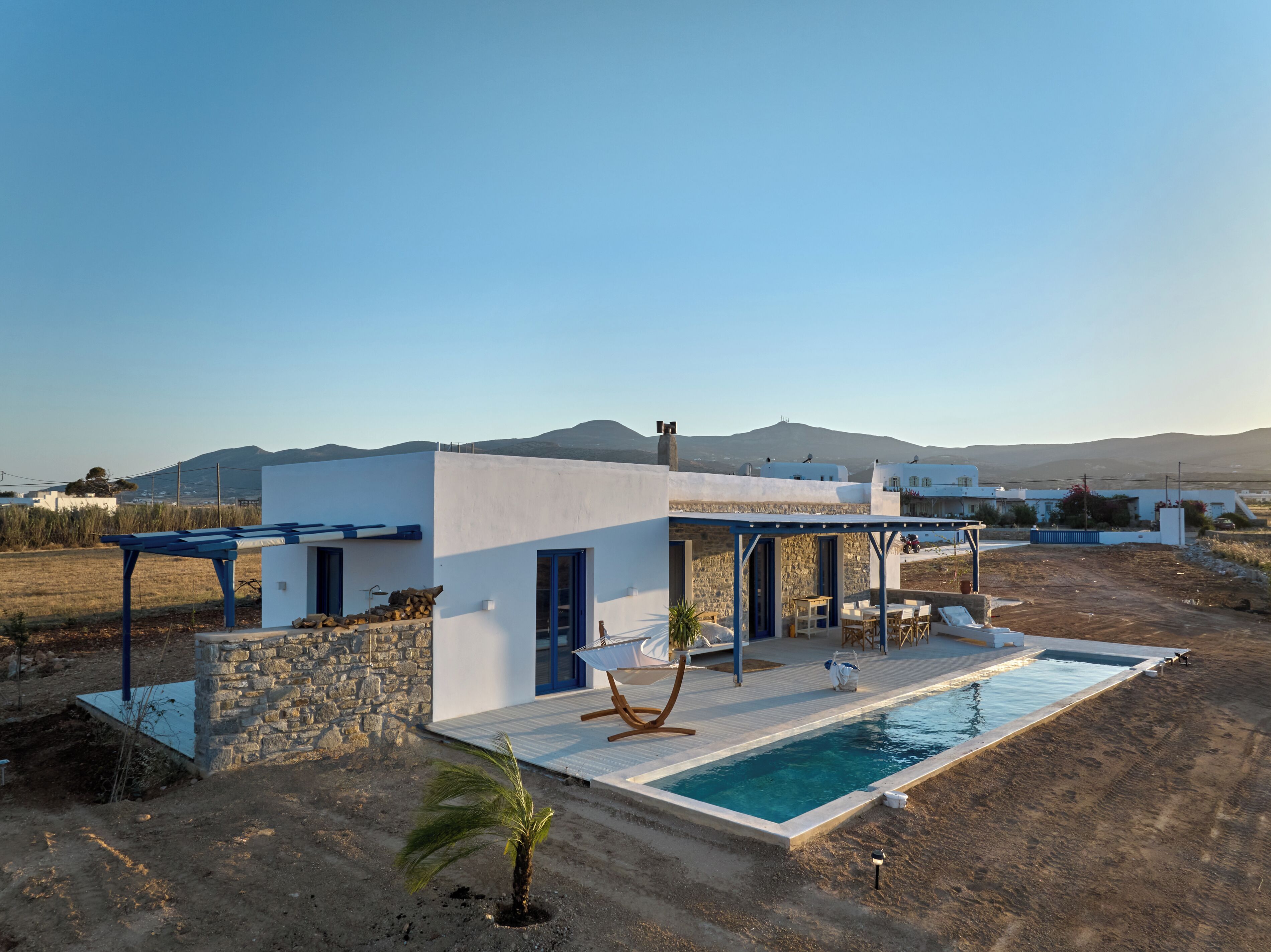 A modern villa with a swimming pool, stone walls, and a view of distant mountains.