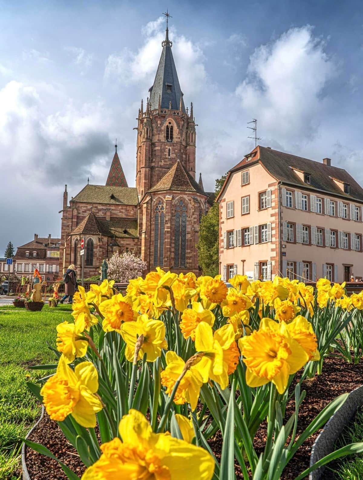 Eine Kirche mit einem hohen Kirchturm und ein Gebäude mit einem geneigten Dach im Vordergrund.