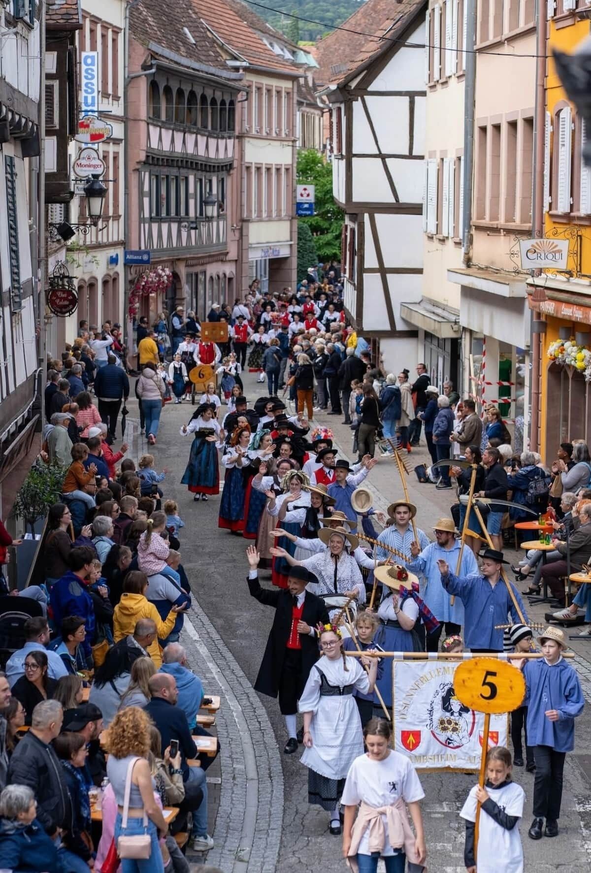 Une rue animée, remplie de personnes vêtues de costumes traditionnels, ce qui laisse supposer qu’un événement culturel ou un festival s’y déroule.