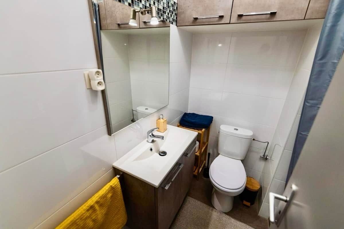Et lille badeværelse med vask, spejl, toilet og en lille træskammel.