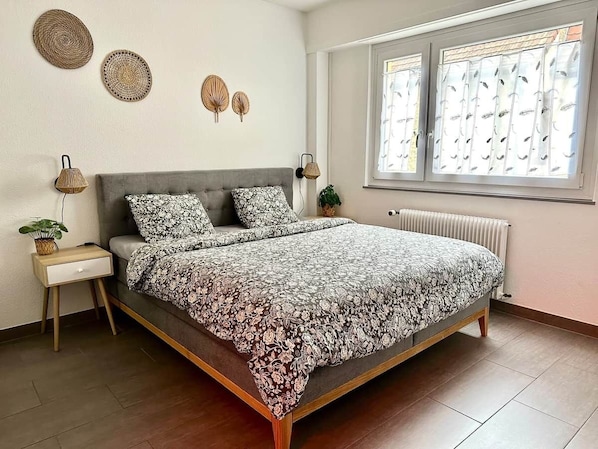 A bedroom with a bed, bedside tables, a radiator, and a window with blinds.