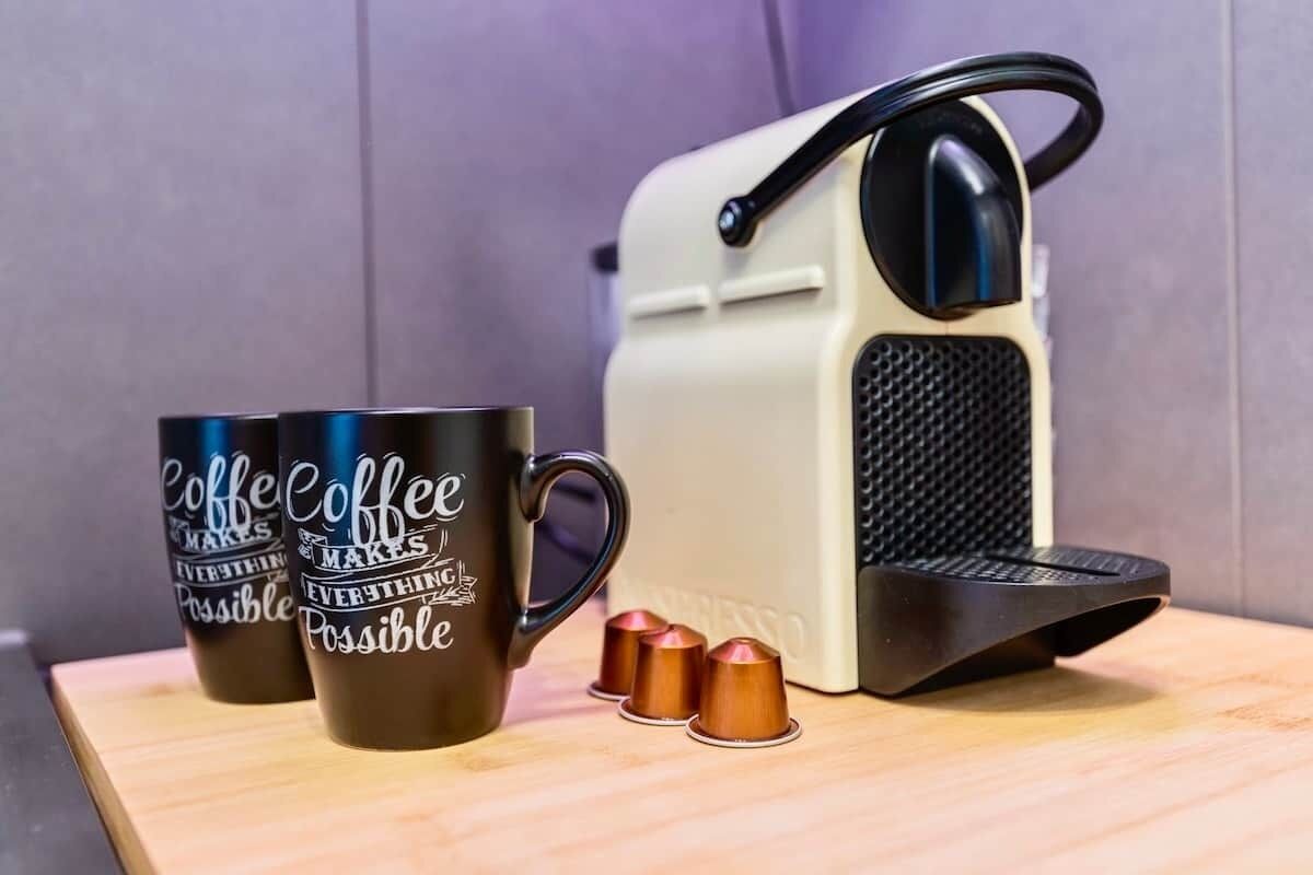 A coffee maker with two cups and three capsules on a wooden surface.