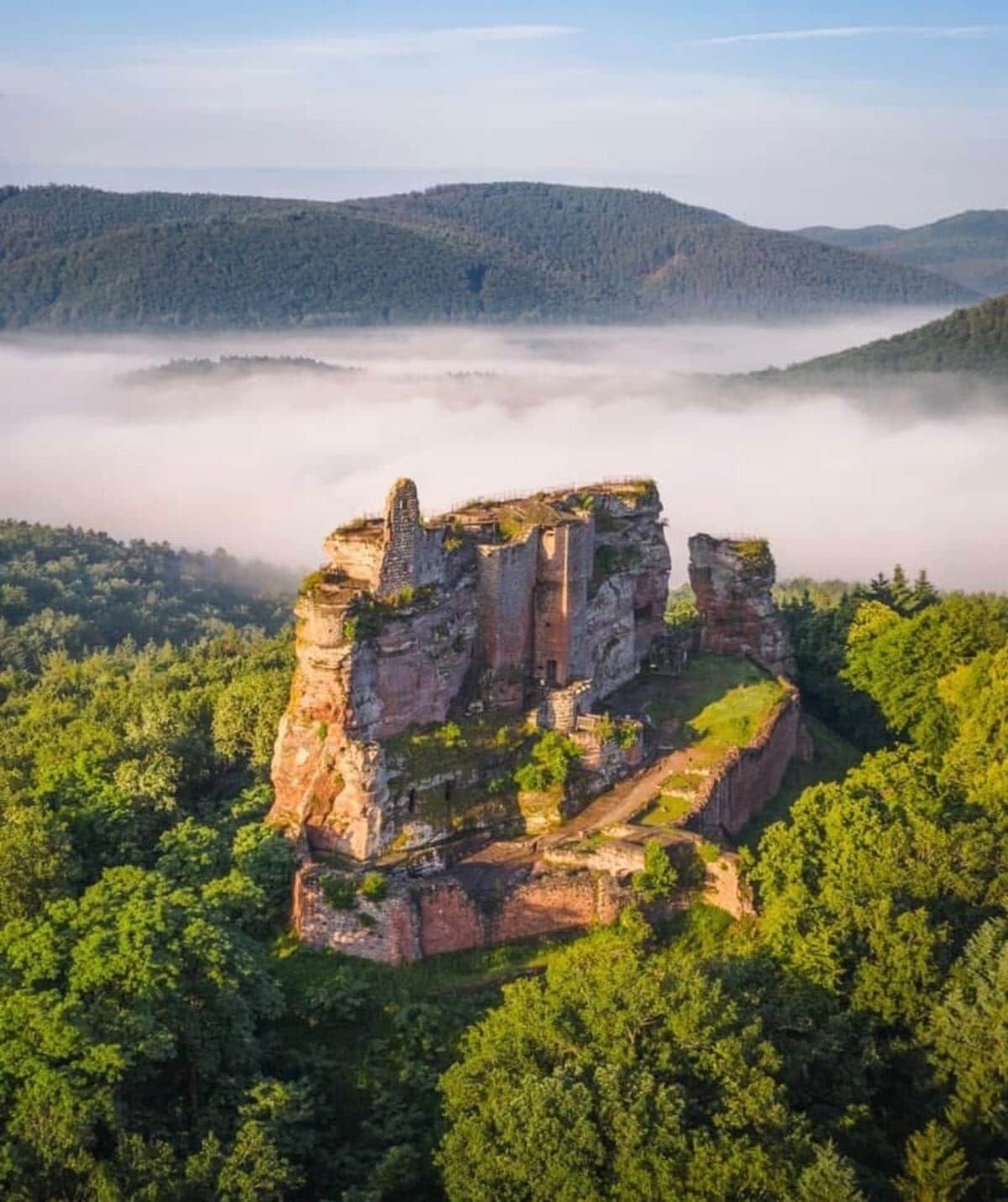 A historic stone structure surrounded by dense forest and mist-covered hills.