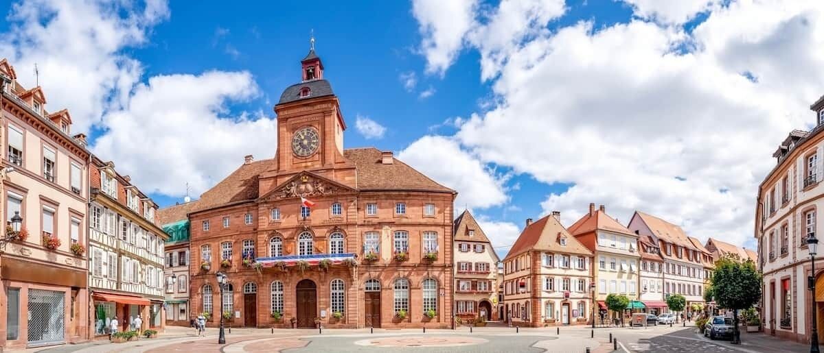 Ein historisches Gebäude mit einem Uhrturm, großen Fenstern und einem zentralen Eingang.