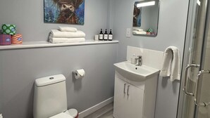 A bathroom with a toilet, sink, and shower. There is a shelf with towels and toiletries.