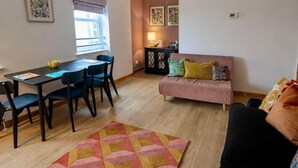 A living area with a sofa, a dining table with chairs, a rug, and a window.
