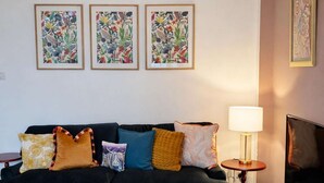 A living room with a black sofa, colorful pillows, a patterned rug, and framed artwork on the wall.