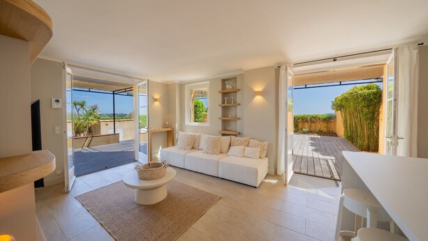 A modern living room with a white sofa, a coffee table, and a dining area with white chairs. There are built-in shelves and a large window offering a view of the outdoors. - Charming house - AC/2 BR/4P - Saint-Tropez (Saint-Tropez)