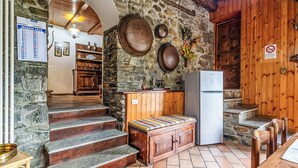 A rustic kitchen with stone walls, wooden furniture, and a stone staircase leading to a dining area. - Moncucco Mountain Home by Interhome (Valtellina)