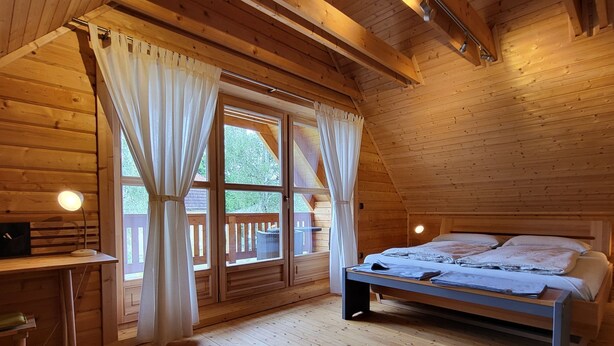 Une chambre dans une cabane en bois, avec un lit, un bureau et une fenêtre avec des rideaux.