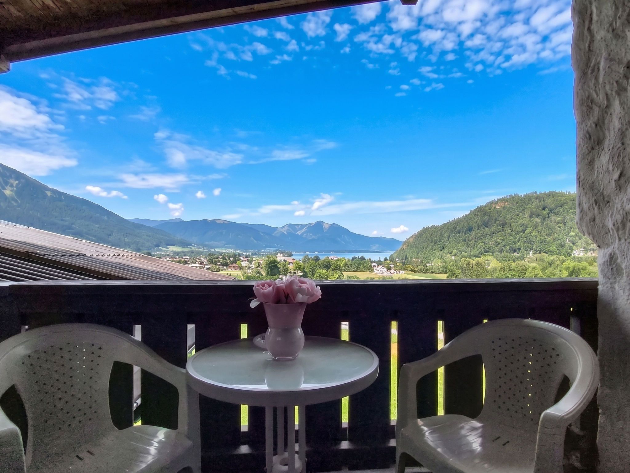 A balcony with a table and chairs, a vase with flowers, and a scenic mountain view.