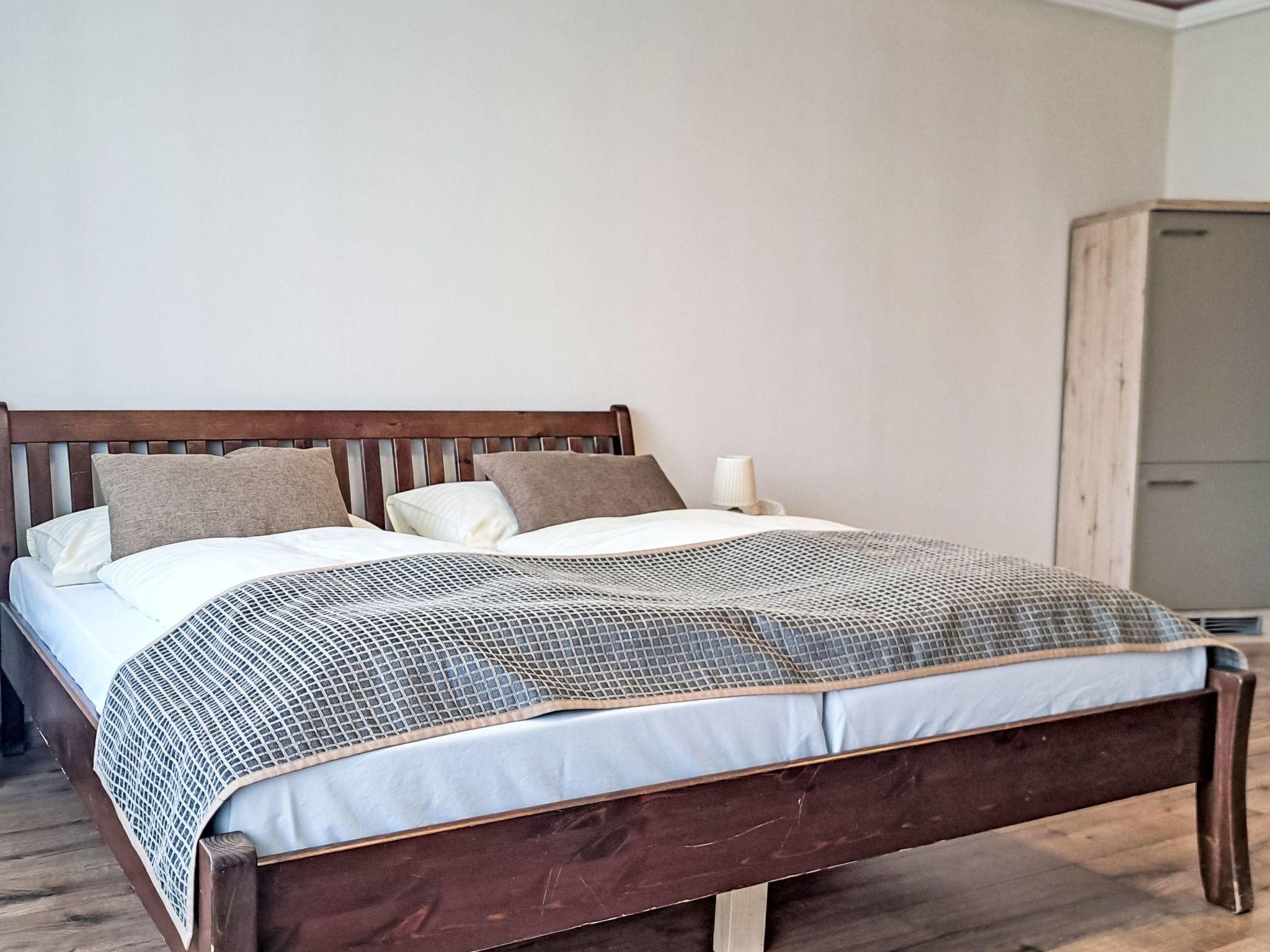 Una cama con estructura de madera, ropa de cama blanca y una colcha estampada.